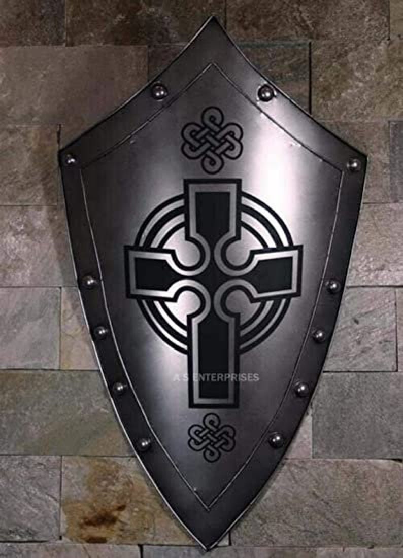 Puede incluir: Un escudo de metal plateado con un dise&ntilde;o de cruz celta negra. El escudo tiene una parte superior puntiaguda y una parte inferior redondeada. Est&aacute; decorado con remaches alrededor del borde.