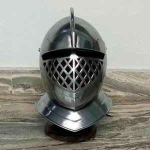 May include: A silver knight's helmet with a visor featuring a diamond-shaped grill pattern. The helmet has a pointed crest and a decorative brim.