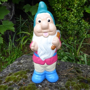 May include: A blue and white garden gnome figurine with a pink shirt and a brown axe. The gnome is smiling and has a white beard.