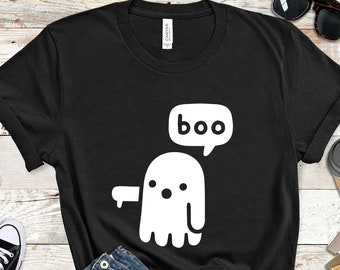 May include: A black short-sleeve t-shirt featuring a white graphic of a ghost with a speech bubble containing the text "boo". The ghost is depicted with a simple rounded shape, two small circular eyes, a small circular mouth, and one arm extended.