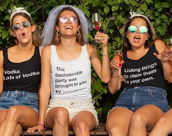 May include: Five women wearing sunglasses and tank tops with humorous phrases, sitting by a pool. The tank tops have phrases like "Bad Decisions" and "Vodka. Lots of Vodka." Pink flamingo pool floats and balloons are in the water.