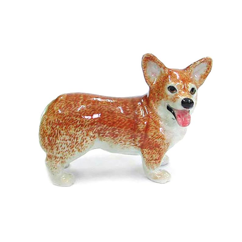 May include: A ceramic corgi figurine with a glossy finish. The dog is depicted in a standing pose, with a reddish-brown coat and white accents on its paws, chest, and face. Its tongue is pink, and its eyes are black.