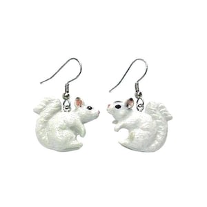 May include: A pair of silver dangle earrings featuring white squirrel charms. The squirrels are facing each other and have black eyes and pink noses.