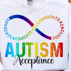 Puede incluir: Sudadera blanca con un símbolo de infinito arcoíris que dice "Advocate, Educate, Accommodate, Include" alrededor. La palabra "AUTISM" está escrita en letras arcoíris debajo del símbolo, y las palabras "Acceptance" están escritas en cursiva debajo de la palabra "AUTISM".