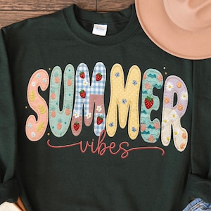Puede incluir: Sudadera verde oscuro con las palabras "SUMMER vibes" en letras coloridas estilo patchwork. Las letras presentan diseños de piñas, cuadros vichy, fresas y margaritas. Un sombrero beige y unos vaqueros son visibles en el fondo.