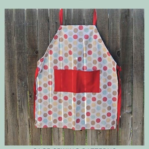 May include: An adjustable strap apron with a polka dot pattern in red, blue, yellow, and brown. The apron has a large red pocket and red straps. The text "ADJUSTABLE STRAP APRON" is at the top.