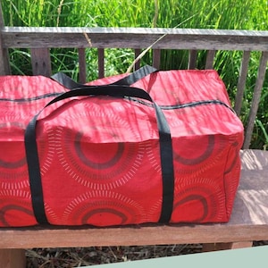 Puede incluir: Bolsa de almacenamiento roja con cremallera, correas negras y un patrón geométrico blanco y rojo. La bolsa está sentada en un banco de madera. "Bolsas de almacenamiento con cremallera" y "Nivel de dificultad: Principiante avanzado" están escritos en blanco sobre un fondo verde claro.