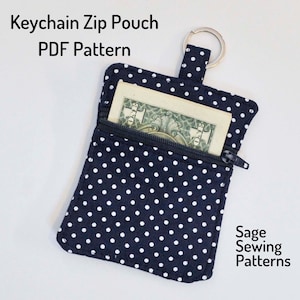 Pode incluir: Uma bolsa de zíper com bolinhas pretas e brancas com um anel de chaveiro prateado. A bolsa está aberta e um dólar é visível dentro. O texto "Keychain Zip Pouch PDF Pattern" e "Sage Sewing Patterns" é visível na imagem.