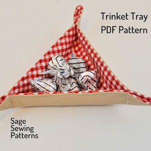 May include: A red and white gingham fabric triangle-shaped trinket tray with a beige fabric lining. The tray is filled with silver foil-wrapped chocolates. The text "Trinket Tray PDF Pattern" is written in black text above the tray. The text "Sage Sewing Patterns" is written in black text below the tray.