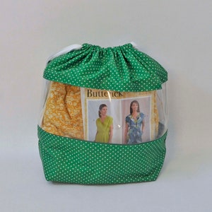 Op de afbeelding: Groene trekkoordtas met witte stippen, met een transparant plastic venster. De tas bevat een naaipatroon met het woord "Butterick" erop gedrukt.