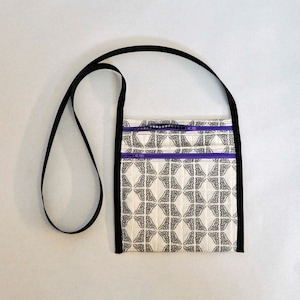 May include: A black and white patterned crossbody bag with a purple zipper. The bag has a black strap and a white background with a black geometric pattern.
