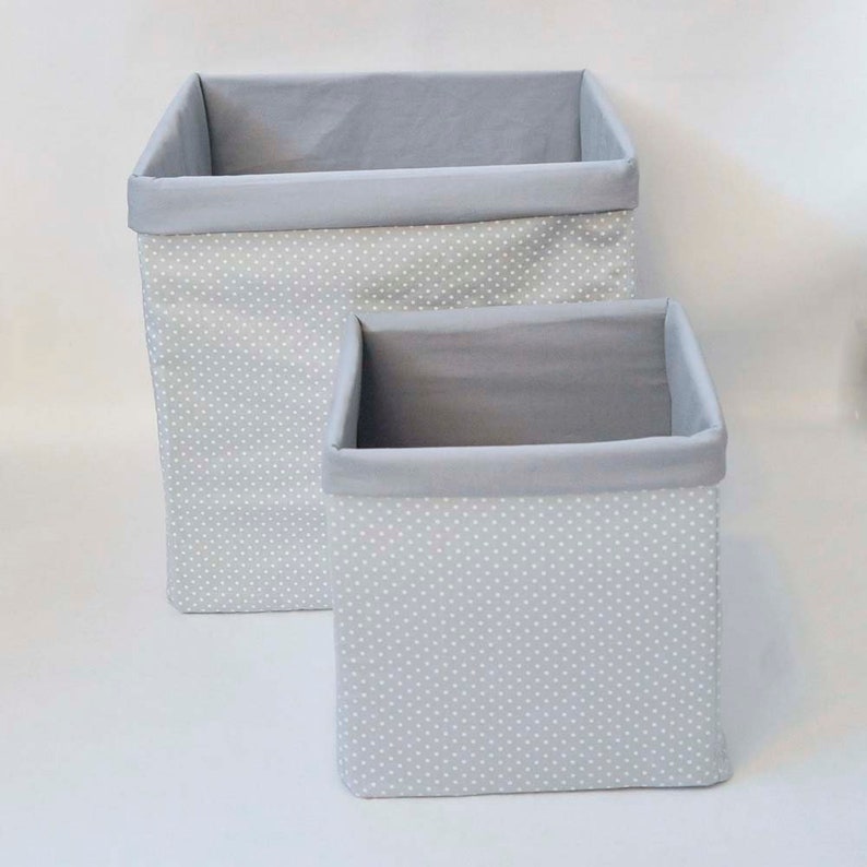 May include: Two gray fabric storage bins with white polka dots. The larger bin is stacked on top of the smaller bin.