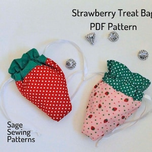 Könnte beinhalten: Zwei stoffene Geschenkbeutel in Form einer Erdbeere mit weißen Kordeln. Ein Beutel ist rot mit weißen Punkten und einem grünen Oberteil. Der andere Beutel ist rosa mit kleinen roten Erdbeeren und einem grünen Oberteil mit weißen Punkten. Die Beutel liegen auf einer weißen Oberfläche mit kleinen silbernen Schokoladen in Folie.