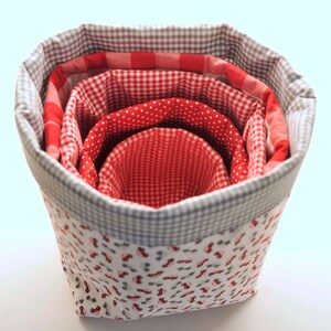 Puede incluir: Un conjunto de cinco cestas de almacenamiento de tela con un patr&oacute;n de cuadros rojos y blancos y un fondo blanco con coches rojos. Las cestas est&aacute;n anidadas una dentro de la otra, con la cesta m&aacute;s grande en la parte inferior y la cesta m&aacute;s peque&ntilde;a en la parte superior.