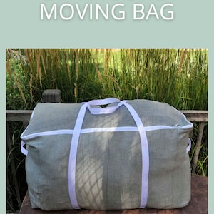 Peut inclure: Un sac de déménagement zippé vert sauge avec des détails et des poignées blancs. Le sac rectangulaire repose sur une surface en bois, avec le texte "ZIP AROUND MOVING BAG" et "SAGE SEWING PATTERNS".