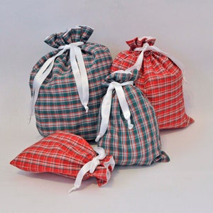 Pode incluir: Quatro sacos de presente em tecido xadrez vermelho e verde com laços brancos. Os sacos estão dispostos em forma de pirâmide.