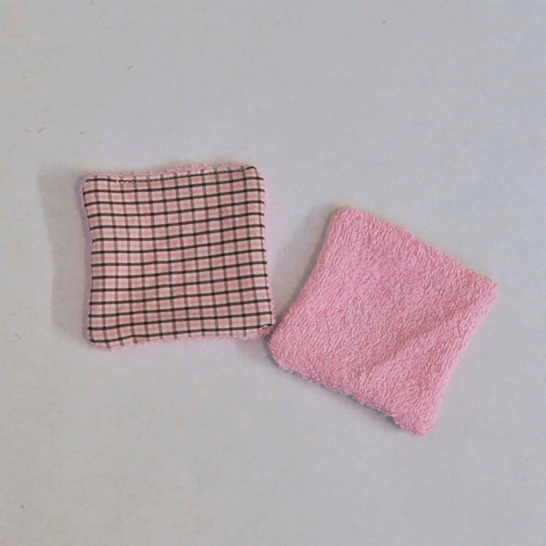 K&ouml;nnte beinhalten: Zwei kleine Waschlappen in Rosa und Braun. Ein Waschlappen ist aus rosa Frottee und der andere aus rosa-braunem kariertem Stoff.