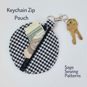 May include: A black and white gingham keychain zip pouch with a zipper closure. The pouch is filled with cash and coins. The pouch is attached to a silver key ring with two keys.