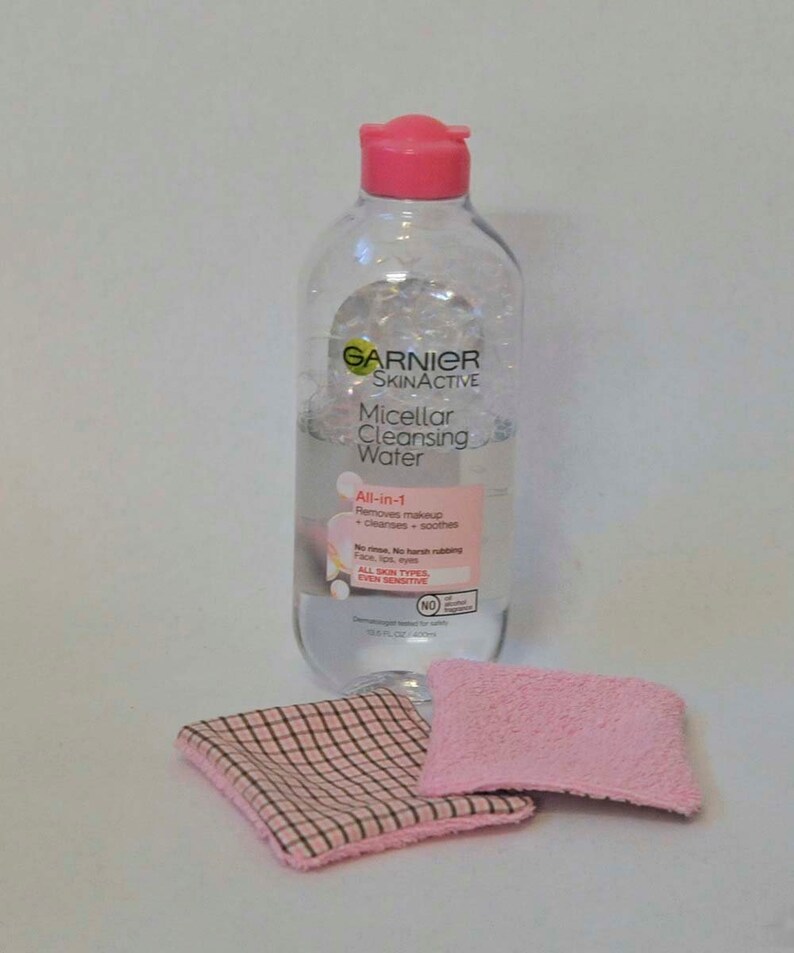 K&ouml;nnte beinhalten: Eine durchsichtige Plastikflasche mit Garnier SkinActive Micellar Cleansing Water. Die Flasche hat einen rosafarbenen Deckel und ein wei&szlig;es Etikett mit dem Produktnamen und der Beschreibung. Die Flasche steht auf einer wei&szlig;en Oberfl&auml;che mit zwei rosa-wei&szlig;en T&uuml;chern.