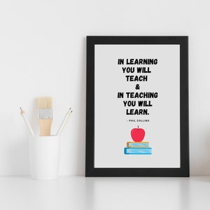 Può includere: Stampa incorniciata in nero con sfondo bianco e una citazione in testo nero: "Nell'apprendimento insegnerai e nell'insegnamento imparerai." - Phil Collins. Una mela rossa e una pila di libri si trovano sotto la citazione.