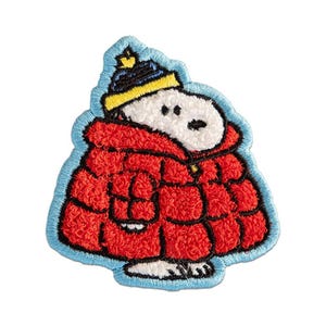 May include: An embroidered patch featuring a white cartoon dog wearing a bright red puffer jacket and a blue and yellow knit hat. The design is outlined in light blue thread, showcasing a textured, raised stitch pattern throughout the entire piece.