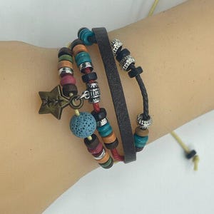 May include: A layered bracelet set with a star charm, brown leather cord, and colorful beads, including a blue lava rock bead.