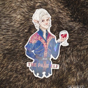 May include: A sticker featuring a stylized illustration of an elf holding a glass of red wine. The elf is dressed in a blue and purple outfit, with the text "THE PALE ELF" at the bottom. The sticker has a holographic effect.