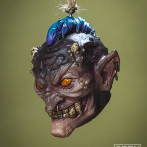 May include: A small, detailed, hand-painted ceramic ornament of a goblin with a purple mohawk, orange eyes, and a gold nose ring. The goblin is hanging from a string.