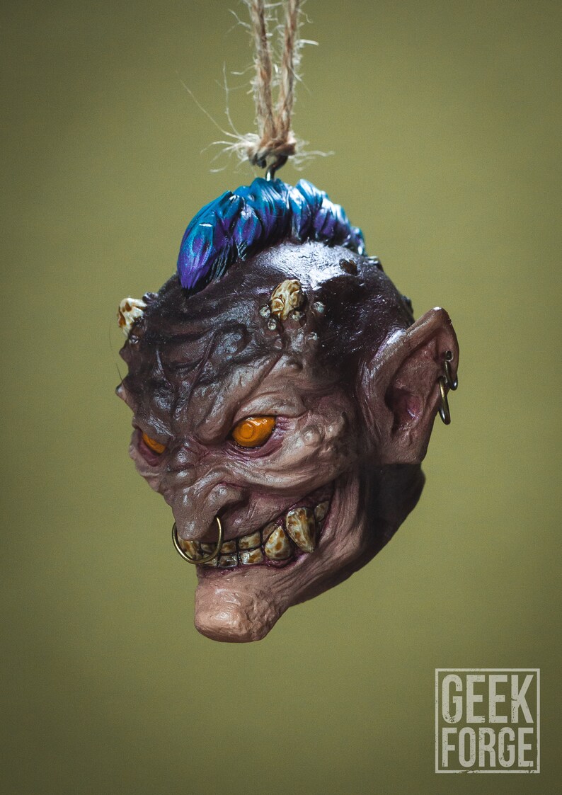 May include: A small, detailed, hand-painted ceramic ornament of a goblin with a purple mohawk, orange eyes, and a gold nose ring. The goblin is hanging from a string.