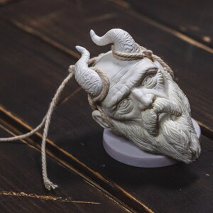 May include: White ceramic sculpture of a bearded man's head with horns, on a wooden surface.