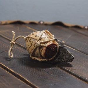 May include: A small, round, brown and white object wrapped in twine with runes inscribed on the surface. The object is tied with a brown rope and has a dark brown, textured, animal-like tail.