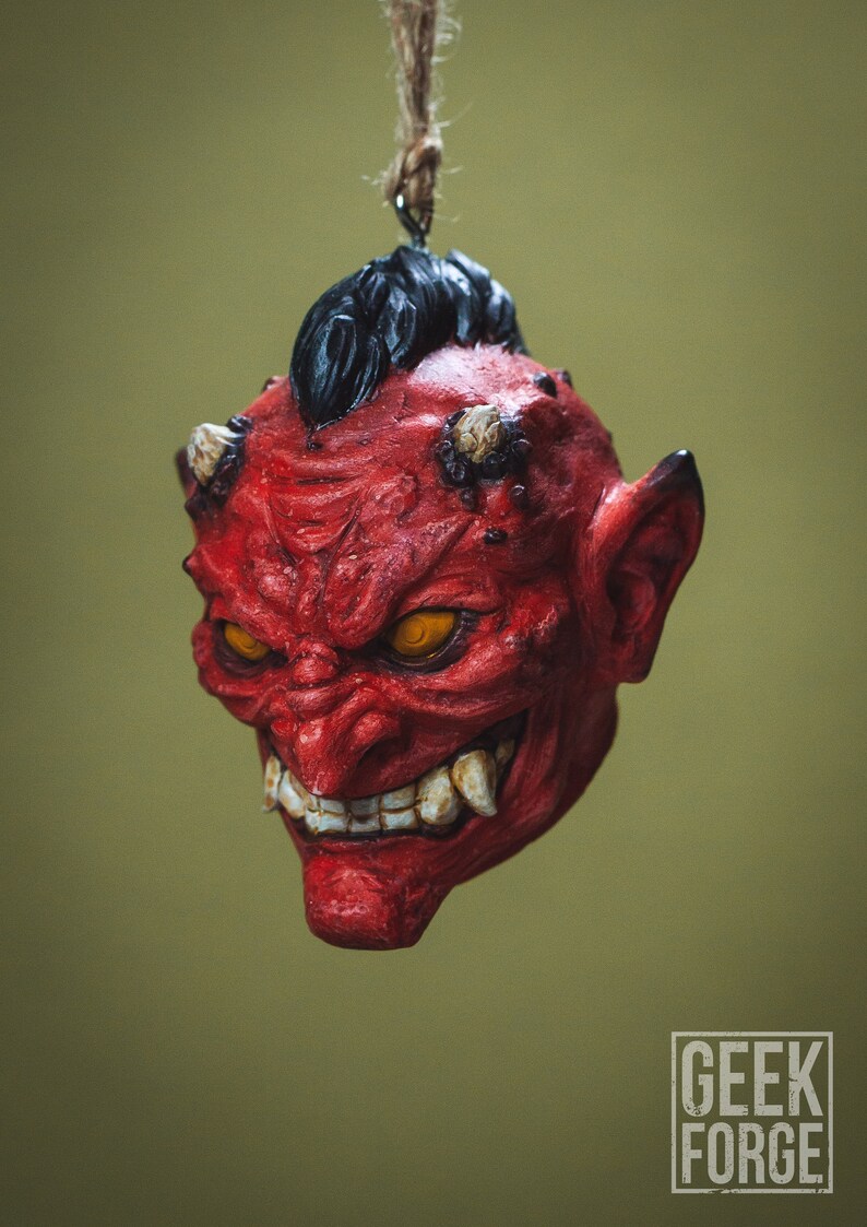 May include: A red and black demon mask with a menacing expression, hanging from a string. The mask has sharp teeth, glowing yellow eyes, and horns.