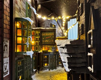 May include: A miniature diorama of a snow-covered street scene with buildings and string lights. The buildings are made of brick and stone, with lit windows and the sign "DERVISH and BANGES". A poster on the left reads "HAVE YOU SEEN THIS WIZARD?"