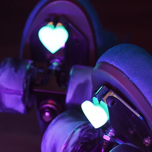 May include: Two roller skate wheels with a glow-in-the-dark heart sticker on each. The wheels are purple and black with a marbled pattern.