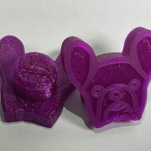 Könnte beinhalten: Zwei lilafarbene 3D-gedruckte Figuren eines französischen Bulldoggen. Die Figuren sind detailliert und haben eine strukturierte Oberfläche.
