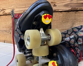 Pode incluir: Patins pretos com rodas amarelas e adesivos de emoji de olhos de coração vermelhos na parte de trás dos patins.