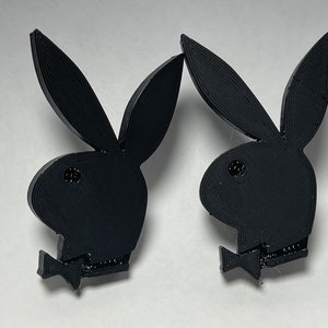 May include: A pair of black 3D printed earrings shaped like the Playboy bunny logo.