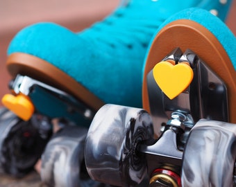 Pode incluir: Um par de patins de rodas turquesa com rodas pretas e topes de dedos em forma de coração amarelo. As rodas têm um padrão de mármore.