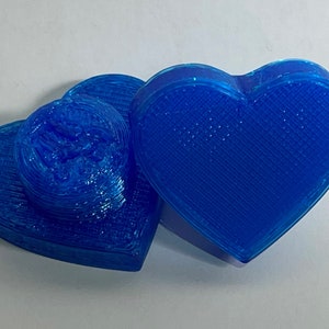 May include: Two blue heart-shaped 3D printed objects. The object on the left is stacked and has a textured surface. The object on the right is a single heart shape.