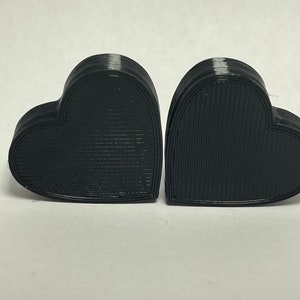 May include: Two black heart-shaped boxes made of 3D printed plastic. The boxes have a textured surface and are stacked on top of each other.