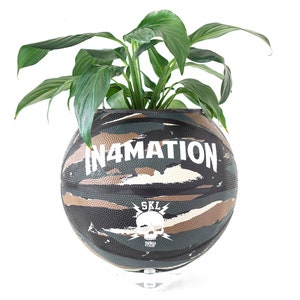 May include: A camouflage-patterned basketball planter with the word "IN4MATION" printed on it. A green plant is growing out of the top of the basketball.