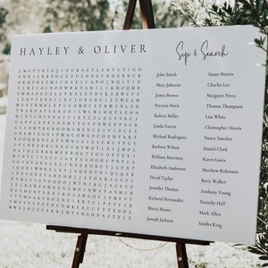 May include: A white sign with the words "Hayley & Oliver Sep 6 Search" at the top. Below the title is a word search puzzle with the names of wedding guests. The names are listed in two columns on the right side of the sign.