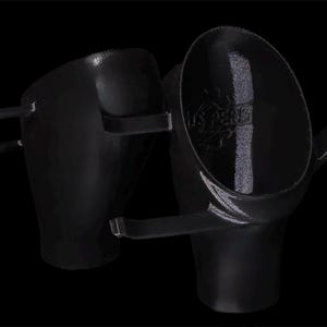 Peut inclure: Deux objets métalliques noirs avec une finition brillante sont présentés sur un fond noir. L'un a une poignée et une forme de bol incurvée, l'autre a deux bras incurvés s'étendant sur le côté.