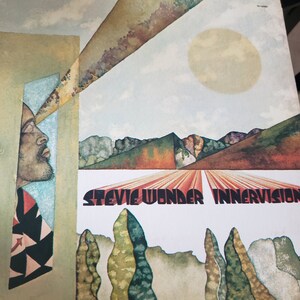 Puede incluir: Una portada de &aacute;lbum de vinilo vintage de Stevie Wonder, "Innervisions". La portada es un dise&ntilde;o abstracto colorido con la cara de un hombre asom&aacute;ndose desde el lado izquierdo de la imagen. El fondo presenta un sol amarillo brillante, un cielo azul y un paisaje con &aacute;rboles y colinas.