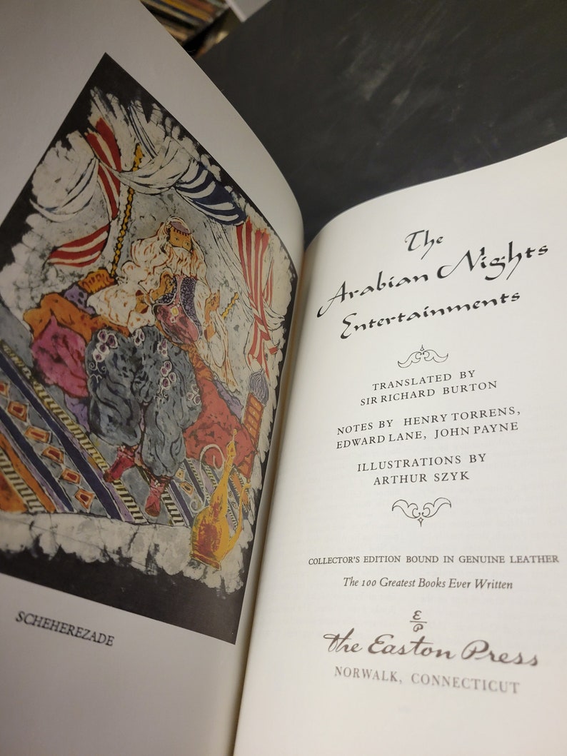 Puede incluir: Una portada de libro con una ilustraci&oacute;n de una escena de "Las Mil y Una Noches" que representa a un hombre con una t&uacute;nica colorida sentado en una alfombra estampada. El texto de la portada dice "Las Mil y Una Noches" e incluye los nombres de los traductores y los ilustradores.