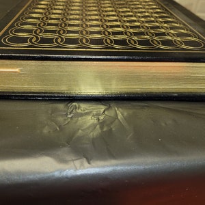 May include: A black leather-bound book with gold-gilded edges and a decorative pattern of interlocking circles on the cover.