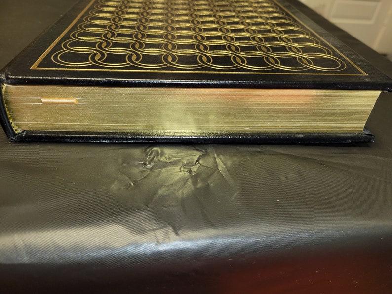 May include: A black leather-bound book with gold-gilded edges and a decorative pattern of interlocking circles on the cover.