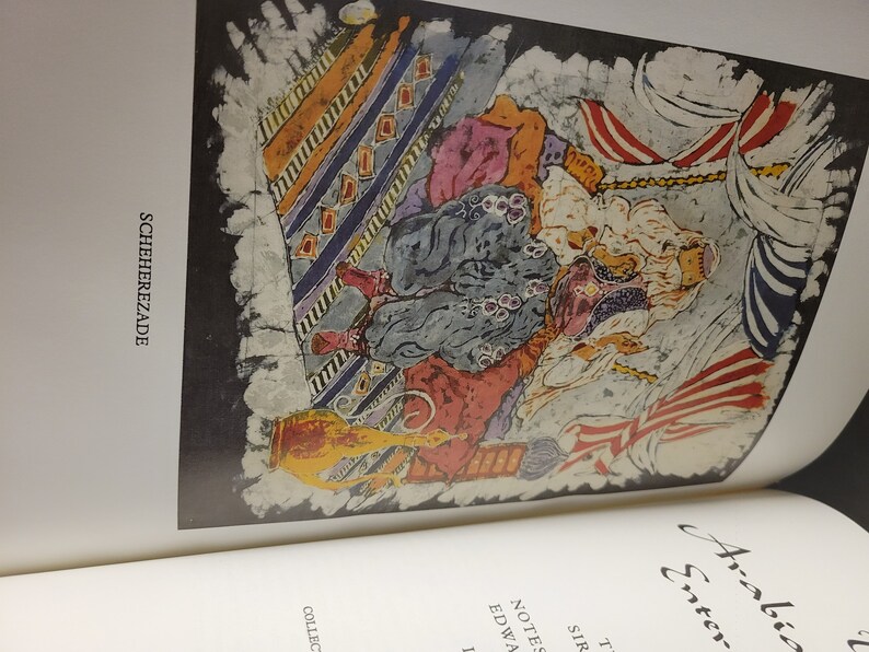 Puede incluir: Una ilustraci&oacute;n colorida de una escena de "Las mil y una noches" con el texto "Scheherezade" y "Arabian Entertainments" visible. La ilustraci&oacute;n presenta a una mujer con una t&uacute;nica azul y roja sentada en una alfombra estampada con un hombre con una t&uacute;nica blanca a su lado. La ilustraci&oacute;n est&aacute; pintada en un estilo vibrante con colores y pinceladas audaces.