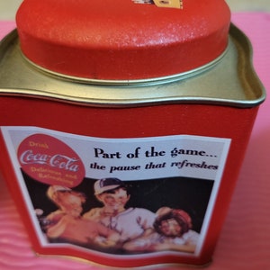 Puede incluir: Lata roja de Coca-Cola con tapa plateada. La lata tiene un logotipo vintage de Coca-Cola y el texto "Drink Coca-Cola Delicious and Refreshing Part of the game... the pause that refreshes". La lata presenta una imagen vintage de tres personas disfrutando de una Coca-Cola.