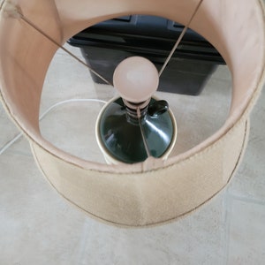 May include: A beige lampshade with a green and white ceramic base. The lampshade is attached to the base with a metal frame.
